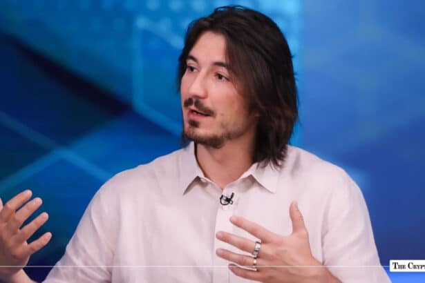Robinhood CEO Tenev gesturing during an interview against a blue geometric background