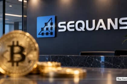 A physical gold Bitcoin coin in the foreground with the Sequans logo mounted on an office wall behind it.