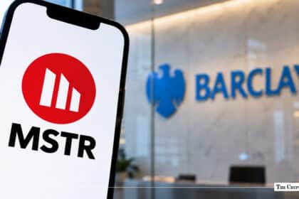 Smartphone displaying the MicroStrategy (MSTR) red circular logo with a blurred Barclays bank logo in the background
