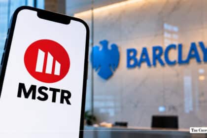 Smartphone displaying the MicroStrategy (MSTR) red circular logo with a blurred Barclays bank logo in the background
