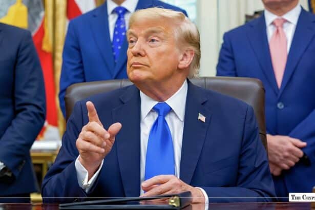Donald Trump speaking with raised index finger while seated at a desk.