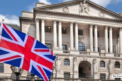 The UK flag flying in front of a classical stone financial building.