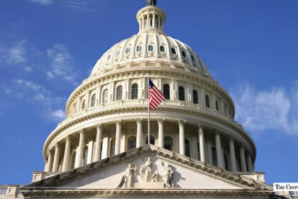Low-angle exterior view of the United States Capitol dome under a clear blue sky with the American flag flying