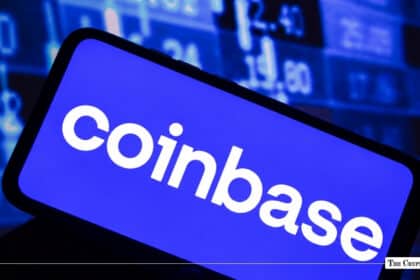 Smartphone displaying Coinbase app logo with financial stock market ticker screen in background