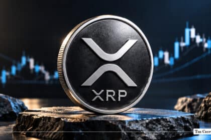 Silver physical XRP coin displayed on a stone pedestal against a blue market chart.