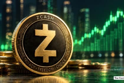 Gold Zcash (ZEC) physical token resting on a reflective surface embossed with "PRIVACY • FREEDOM • CHOICE" against a green upward-trending chart