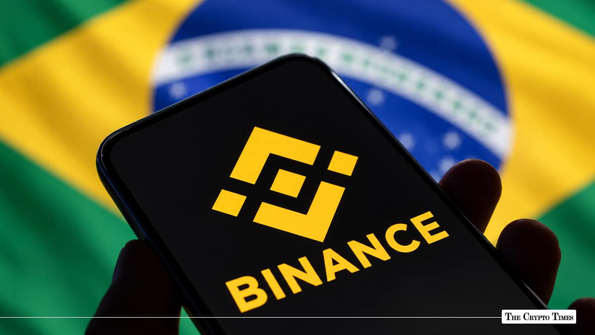 Smartphone displaying yellow Binance logo in hand with Brazilian flag in background