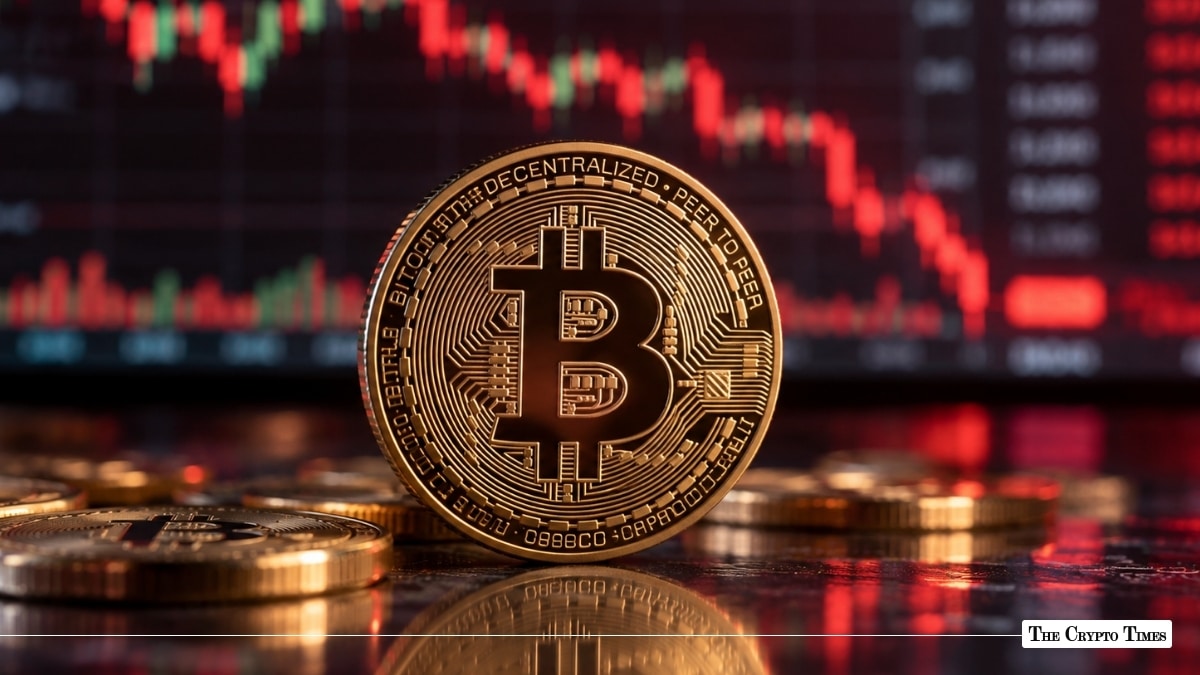 Physical gold Bitcoin coin standing upright in front of a falling red market chart.