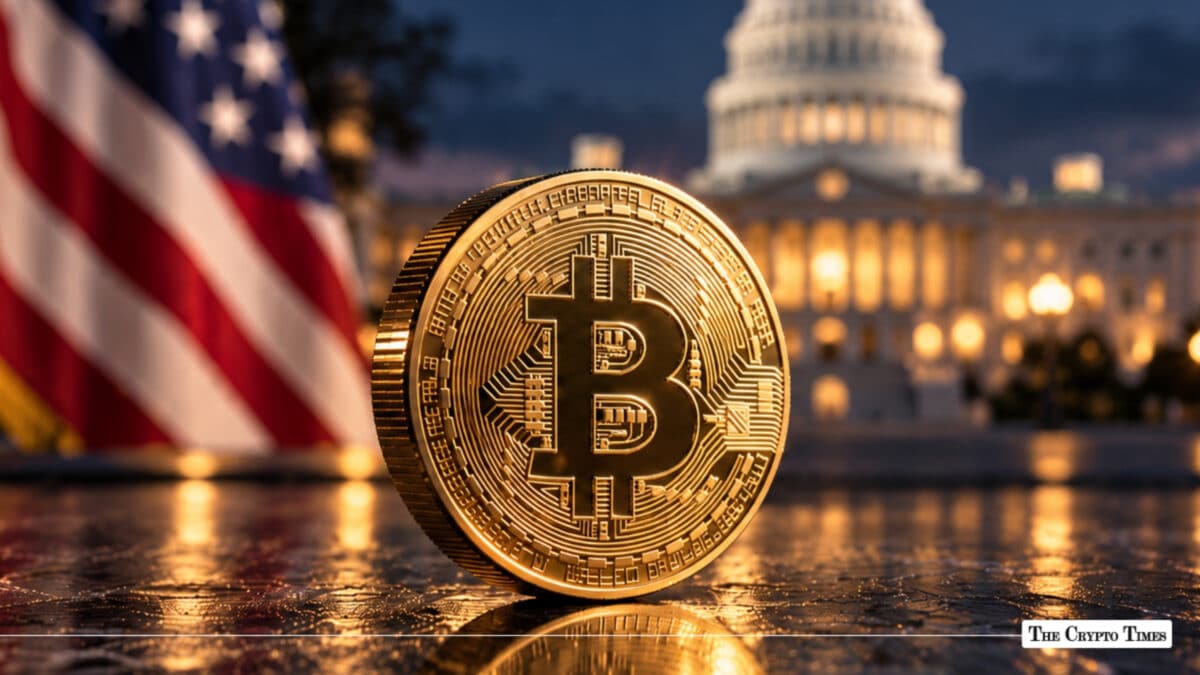 A physical gold Bitcoin coin standing on a reflective surface with the U.S. Capitol building and American flag blurred in the background.