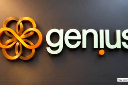 Genius Group corporate logo featuring a golden multi-loop floral emblem alongside lower-case white typography on a dark gray wall