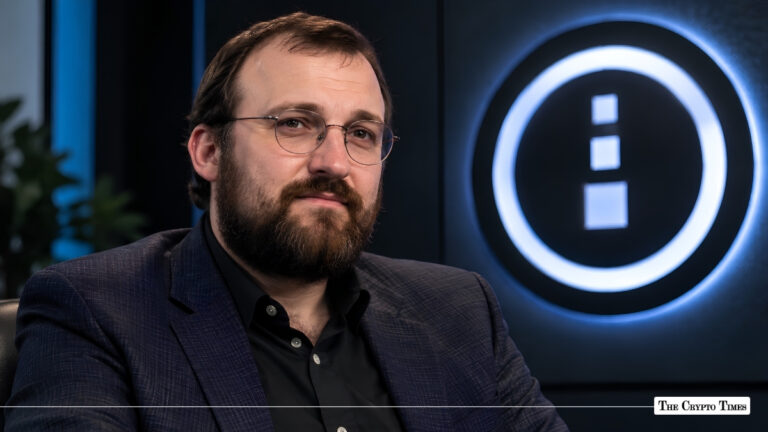 Charles Hoskinson wearing glasses and a suit jacket seated in front of an IOHK logo backdrop.