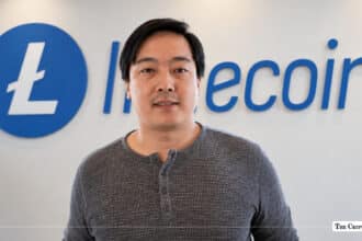 Charlie Lee, creator of Litecoin, standing in front of a blue Litecoin corporate logo wall