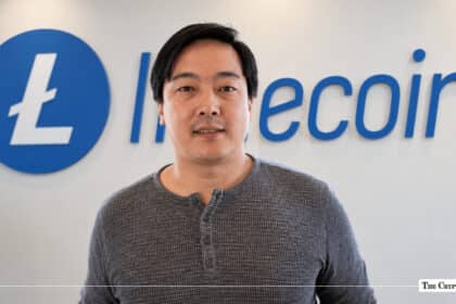 Charlie Lee, creator of Litecoin, standing in front of a blue Litecoin corporate logo wall