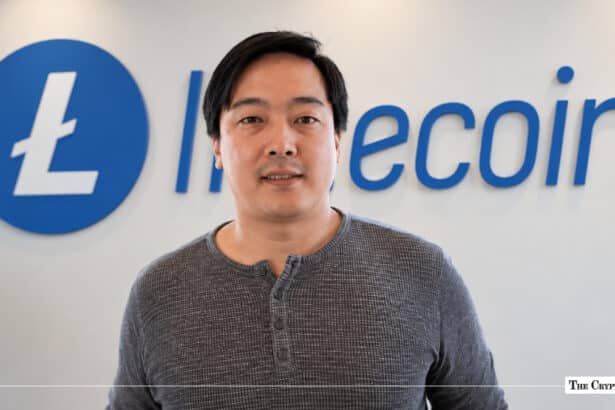 Charlie Lee, creator of Litecoin, standing in front of a blue Litecoin corporate logo wall