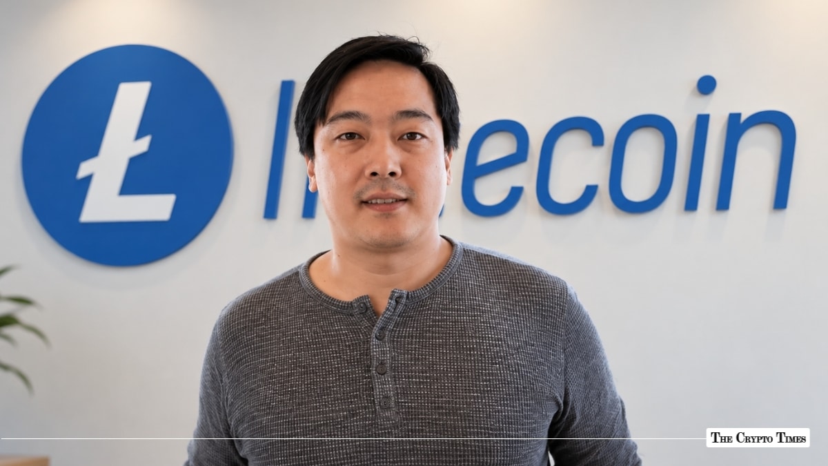 Charlie Lee, creator of Litecoin, standing in front of a blue Litecoin corporate logo wall