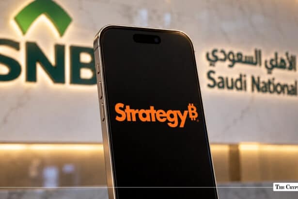 Smartphone displaying MicroStrategy logo in front of Saudi National Bank SNB wall logo