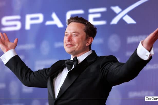 Elon Musk in a tuxedo gesturing with raised arms in front of a SpaceX banner backdrop