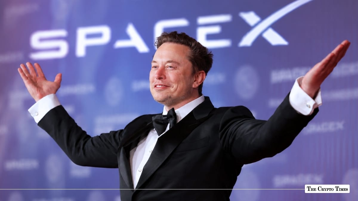 Elon Musk in a tuxedo gesturing with raised arms in front of a SpaceX banner backdrop