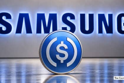 Physical USD Coin (USDC) token standing in front of an illuminated Samsung corporate wall sign