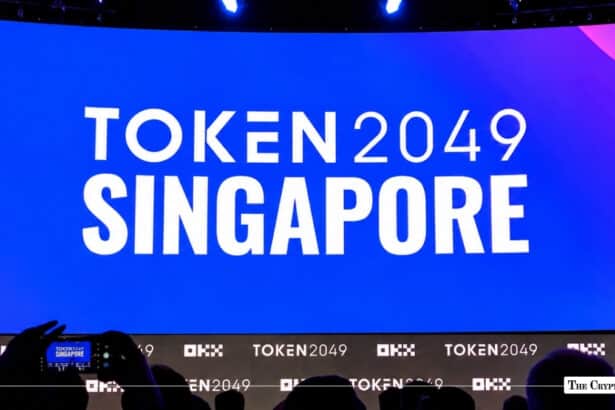 TOKEN2049 Singapore event backdrop illuminated in white text on a bright blue stage screen above an audience silhouette