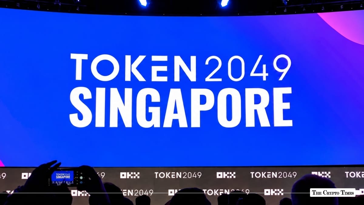 TOKEN2049 Singapore event backdrop illuminated in white text on a bright blue stage screen above an audience silhouette