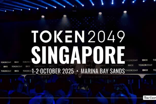 TOKEN2049 Singapore event backdrop on a dark stage displaying "1-2 October 2025 • Marina Bay Sands" with blue spotlights and audience silhouettes below