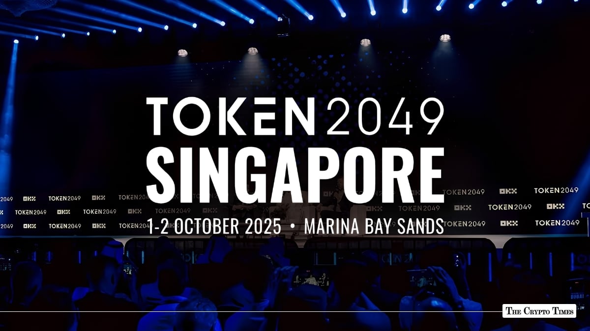 TOKEN2049 Singapore event backdrop on a dark stage displaying "1-2 October 2025 • Marina Bay Sands" with blue spotlights and audience silhouettes below