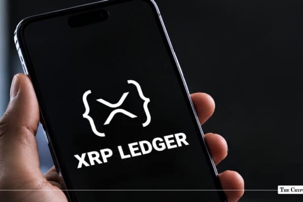 Hand holding a smartphone displaying the XRP Ledger logo and text.